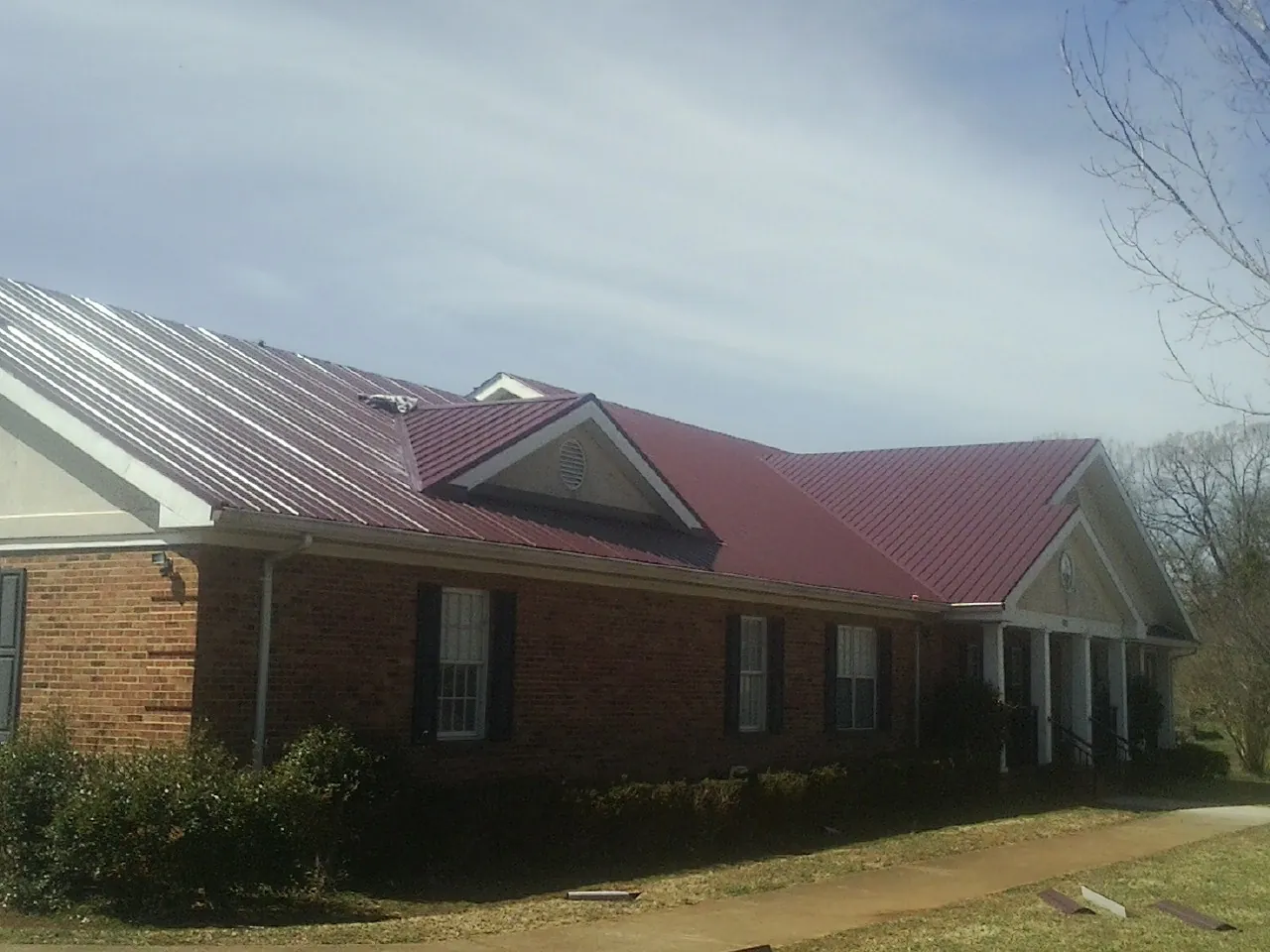 Red metal roof with gabled entries on a long brick building, from a Hail Damage Roof Repair job in Leonardtown