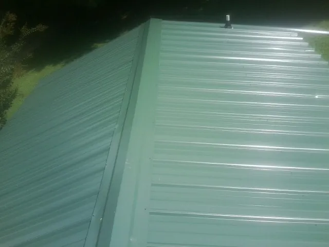 New green metal panels meeting at the ridge of a roof — Flat Roof Repair work by our crew in Leonardtown