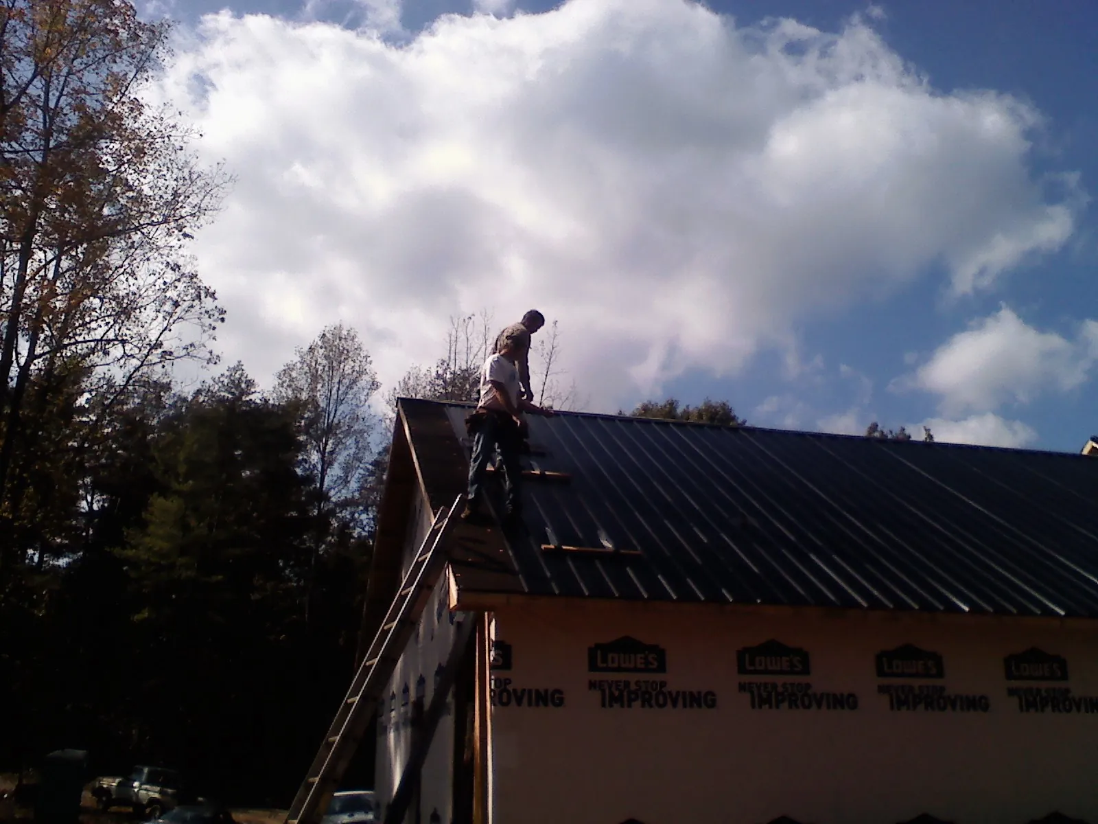 Roofer fastening dark metal panels high against a cloudy sky, from a Roof Inspection job in Leonardtown