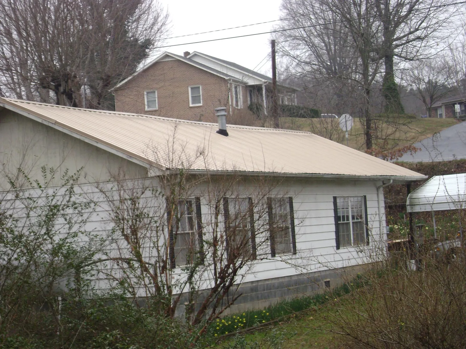 Tan metal roof on a white sided house set into a hillside — Commercial Roofing by Roofing Brothers in Leonardtown